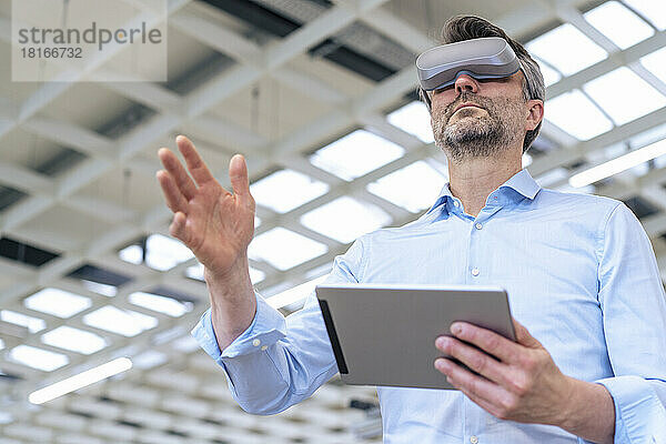 Geschäftsmann mit Virtual-Reality-Simulator gestikuliert und hält Tablet-PC in der Industrie