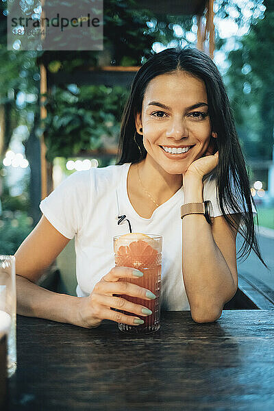 Glückliche Frau mit einem Glas Cocktail  die am Tisch im Straßencafé sitzt