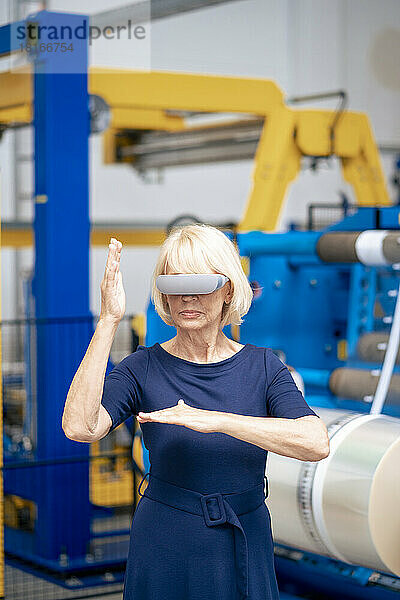 Ältere Geschäftsfrau gestikuliert mit Virtual-Reality-Simulatoren in der Fabrik