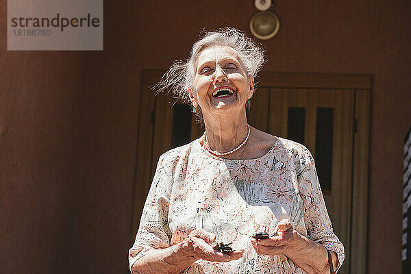 Ältere Frau mit Autoschlüsseln lacht an sonnigem Tag