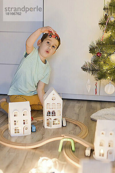 Netter Junge spielt mit Miniatur-Eisenbahnspielzeug in der Nähe des Weihnachtsbaums zu Hause