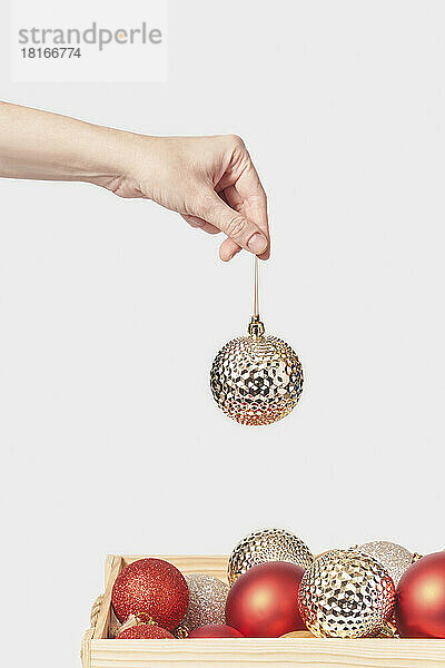 Hand of woman holding golden bauble against white background