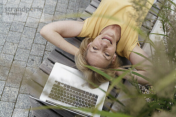 Glückliche reife Frau entspannt sich am Laptop auf der Bank