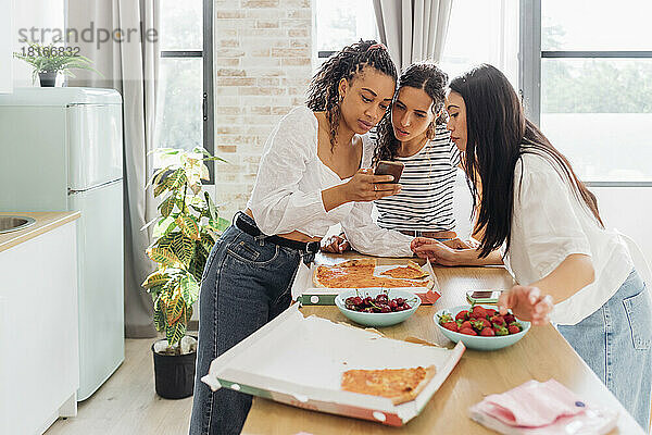 Young woman sharing smart phone with friends in kitchen
