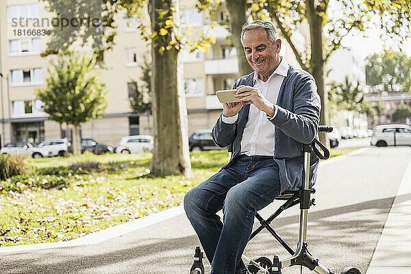 Glücklicher älterer Mann  der sein Smartphone benutzt und auf einem Rollator sitzt