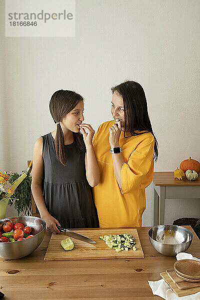 Mutter und Tochter essen zu Hause Gemüse