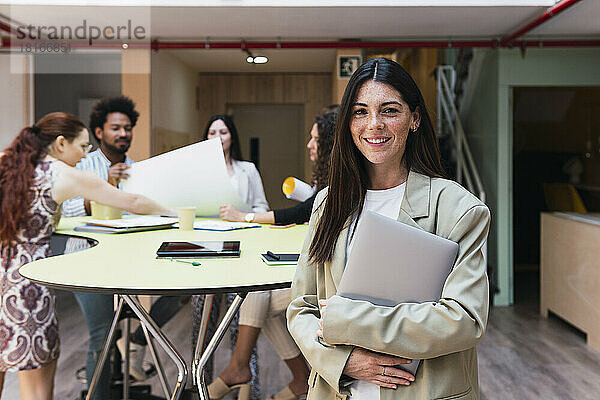 Porträt einer lächelnden brünetten Geschäftsfrau mit Laptop im Büro