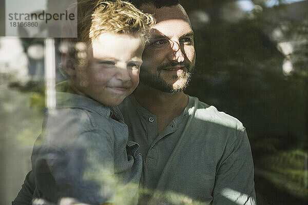 Vater hält Sohn auf dem Arm und schaut durchs Fenster