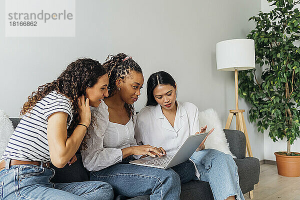 Frau macht Online-Einkäufe am Laptop mit Freunden im Wohnzimmer