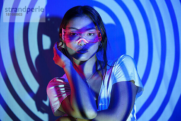 Junge Frau mit LED-Brille steht vor der Wand im spiralförmigen Schatten