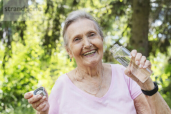 Glückliche ältere Frau hält Wasserflasche im Park
