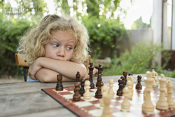 Nachdenkliches Mädchen mit blonden Haaren blickt auf das Schachbrett auf dem Tisch