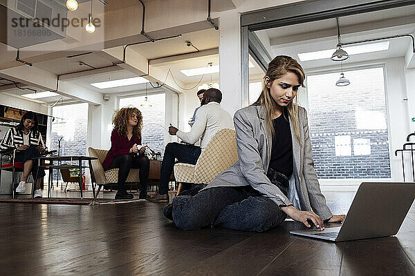 Junge Geschäftsfrau sitzt mit Laptop auf der Büroetage