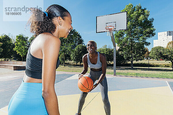 Happy sportswomen playing basketball in court on sunny day