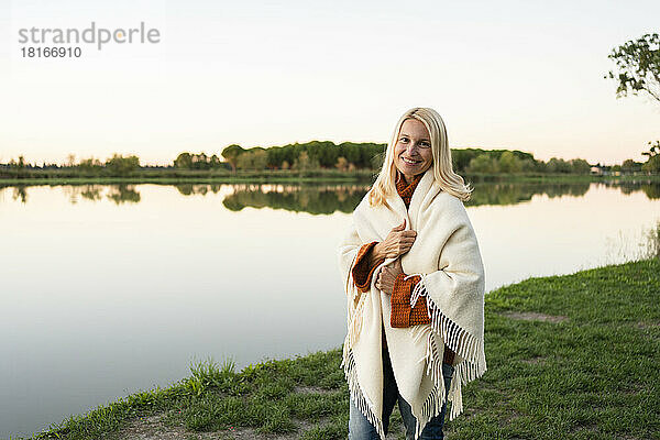 Lächelnde Frau  in eine Decke gehüllt  steht am See