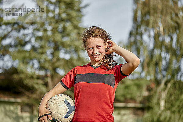 Happy girl with soccer ball standing in front of trees