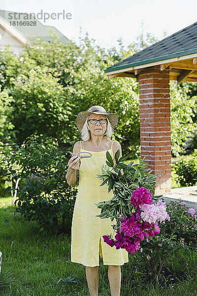 Frau hält Gartenschere und Blumen im Garten