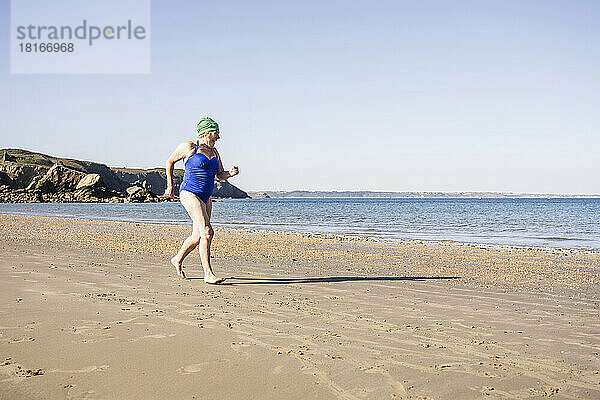 Frau im Badeanzug joggt am Strand