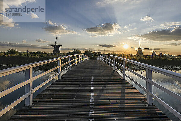 Niederlande  Südholland  Kinderdijk  Landschaftsbrücke bei Sonnenuntergang mit historischen Windmühlen im Hintergrund