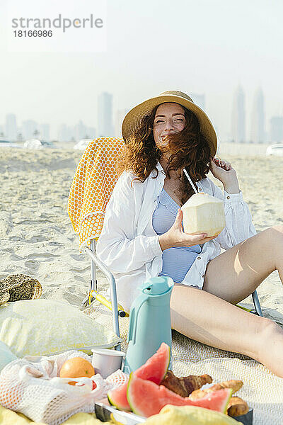 Glückliche Frau mit Kokosnuss genießt sonnigen Tag am Strand