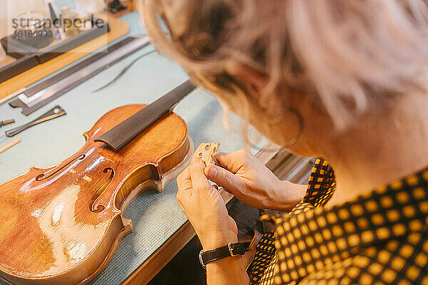 Gitarrenbauer mit Handwerkzeug  das Holz am Schreibtisch in der Werkstatt schnitzt