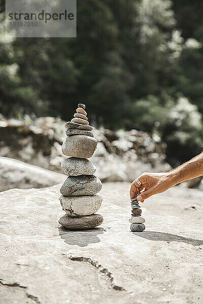 Hand eines Mannes  der Steine ??auf einem Felsen stapelt