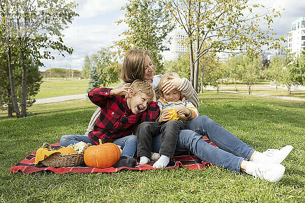 Happy boys with mother sitting on picnic blanket at park