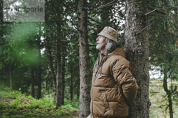 Nachdenklicher Mann steht am Baum im Wald