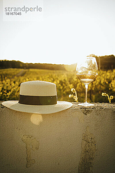 Hat and glass of white wine on wall at sunset