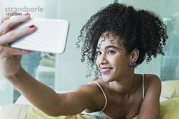 Glückliche schöne Frau mit lockigem Haar  die zu Hause ein Selfie mit dem Smartphone macht