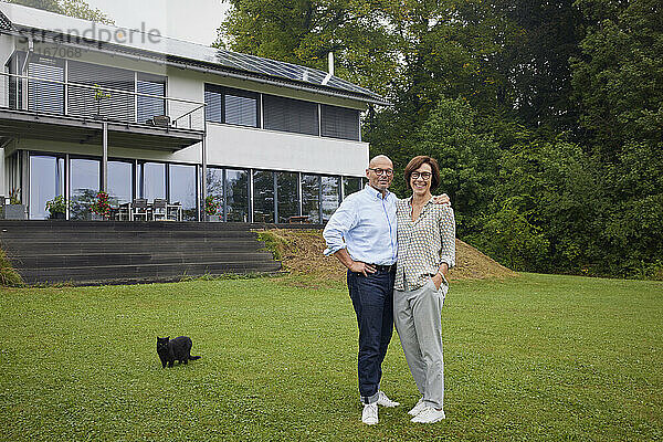 Happy senior man and woman with cat standing in front of house