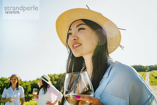 Lächelnde Frau mit Hut und Weinglas an einem sonnigen Tag