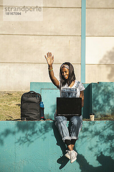 Glücklicher Freiberufler  der an einem sonnigen Tag mit Laptop sitzt und gestikuliert