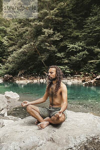 Nackter Oberkörper junger Mann meditiert auf einem Felsen