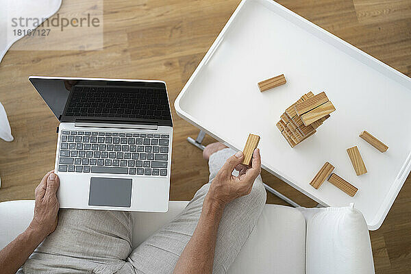 Hand of mature man holding laptop and playing with toy blocks at home