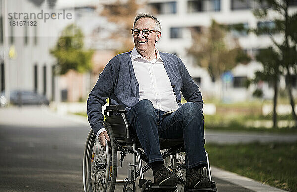 Glücklicher älterer Mann  der im Rollstuhl in der Stadt sitzt