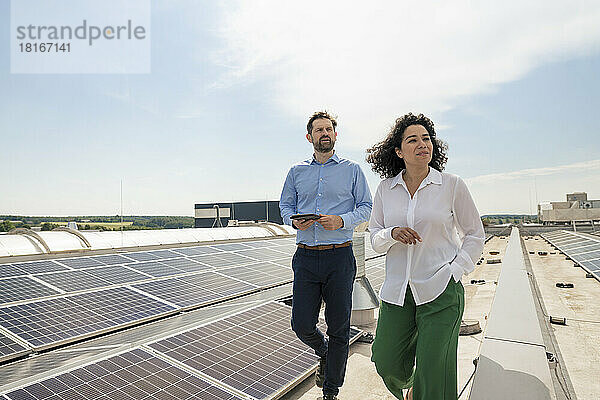 Geschäftsfrau und Geschäftsmann laufen an Sonnenkollektoren auf dem Dach vorbei