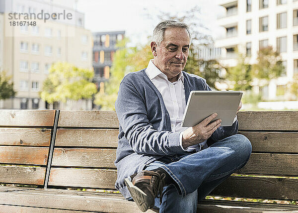 Älterer Mann benutzt Tablet-Computer auf Bank sitzend