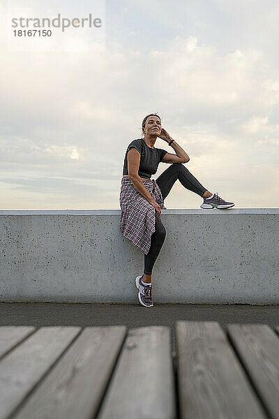 Reife Frau in Sportkleidung sitzt an der Wand vor dem Himmel