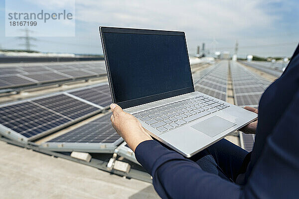 Hände einer älteren Geschäftsfrau  die einen Laptop vor Sonnenkollektoren hält