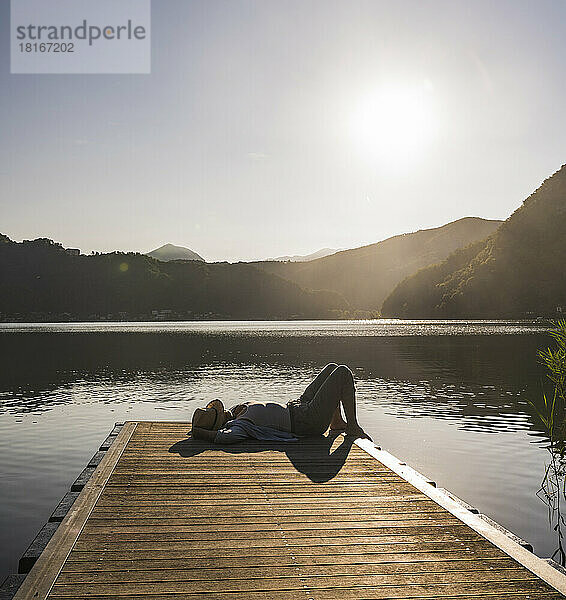 Woman lying on jetty over lake by mountains