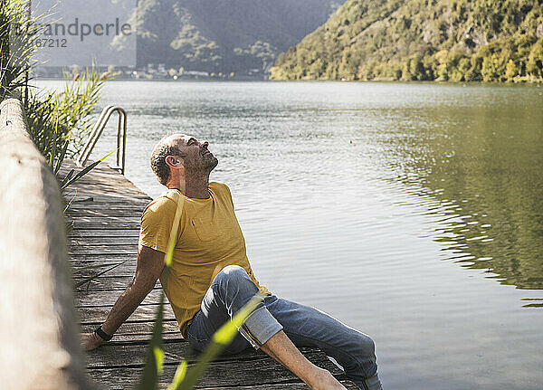 Man relaxing with eyes closed on jetty by lake