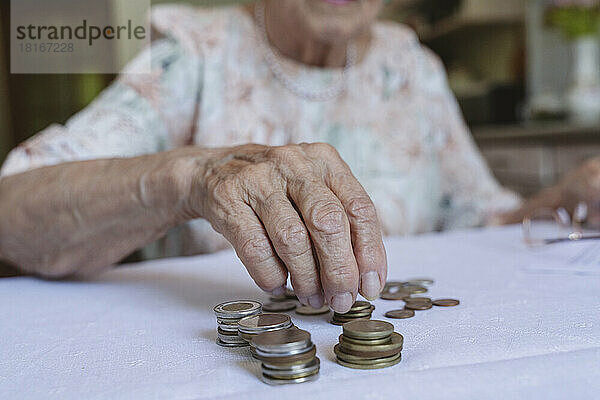 Ältere Frau stapelt zu Hause Münzen auf dem Tisch