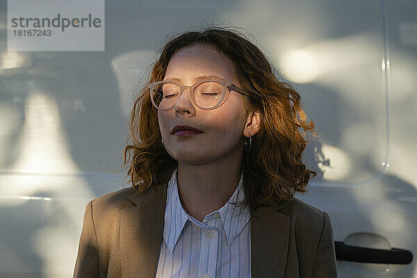 Junge Geschäftsfrau mit geschlossenen Augen im Sonnenlicht
