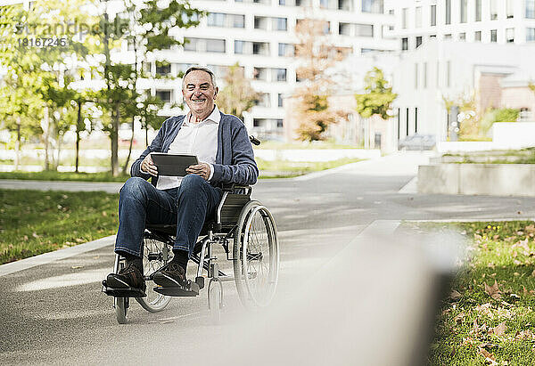 Lächelnder älterer Mann mit Tablet-PC sitzt im Rollstuhl