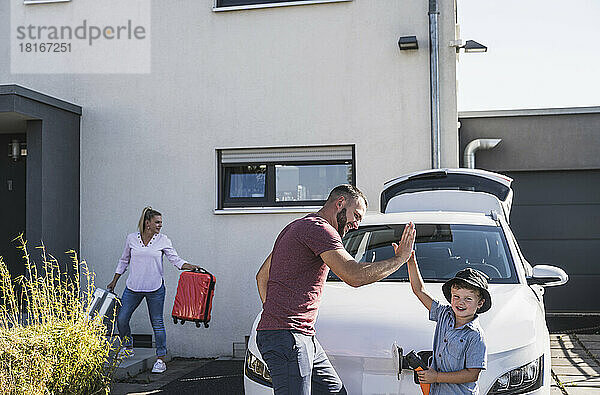 Glücklicher Vater und Sohn beim High-Five vor dem Elektroauto