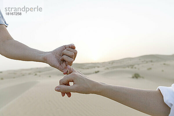 Hände eines Paares  das bei Sonnenuntergang kleine Finger in der Wüste hält