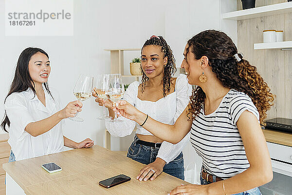 Smiling friends toasting wineglasses in kitchen