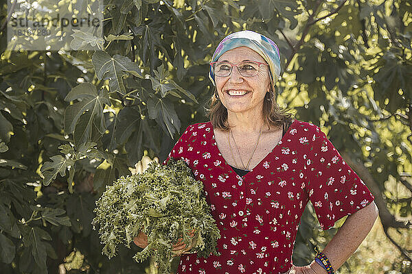 Nachdenkliche Frau mit frischem Rucola vor Pflanzen auf dem Bauernhof