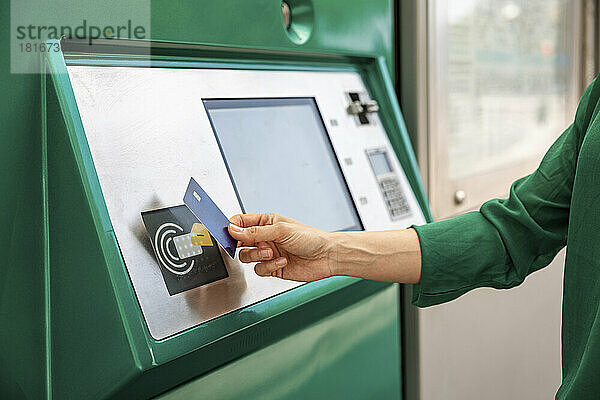 Hand einer Frau  die an der Straßenbahnhaltestelle ihre Kreditkarte am Fahrkartenautomaten tippt